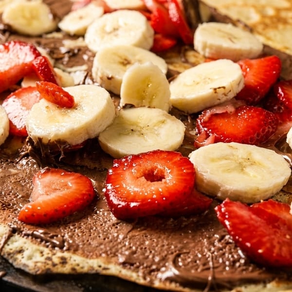 Close-up of a crepe covered in chocolate spread, sliced strawberries, and bananas.