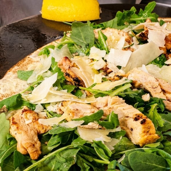 Savory crepe with grilled chicken, fresh arugula, and shaved Parmesan cheese on a griddle.