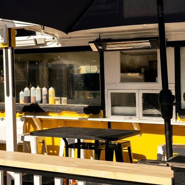 Outdoor seating area with black tables and white stools next to a bright yellow food stand.
