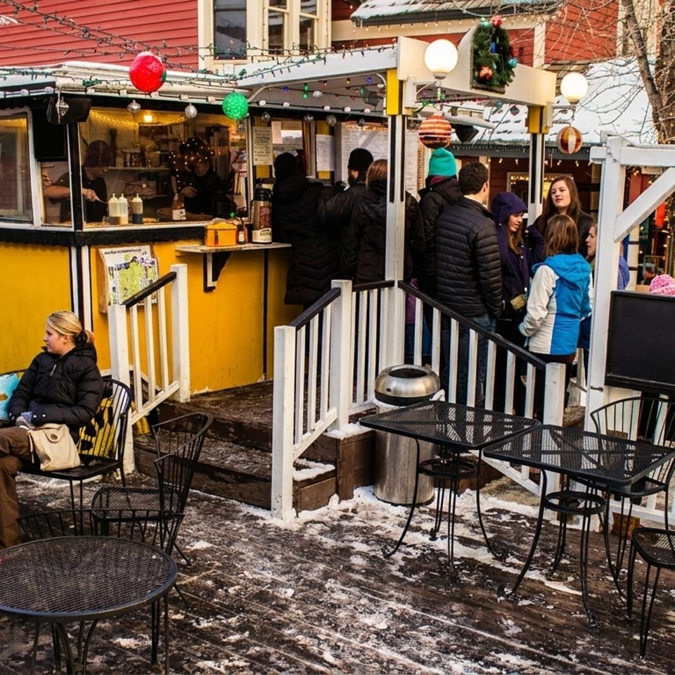 People gather around a yellow "Crêpes à la Cart" food stand with outdoor seating on a snowy day.