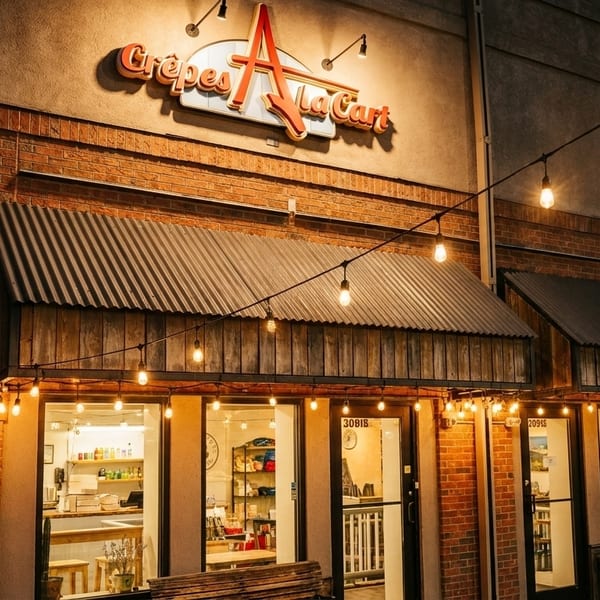 Exterior of Crêpes A La Cart at night, with string lights illuminating the brick facade.